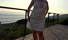 สาวใหญ่นมโตในชุดผ้าซาตินสีขาวมีส่วนร่วมในกิจกรรมทางเพศกลางแจ้งบนระเบียงในช่วงพระอาทิตย์ตกดิน